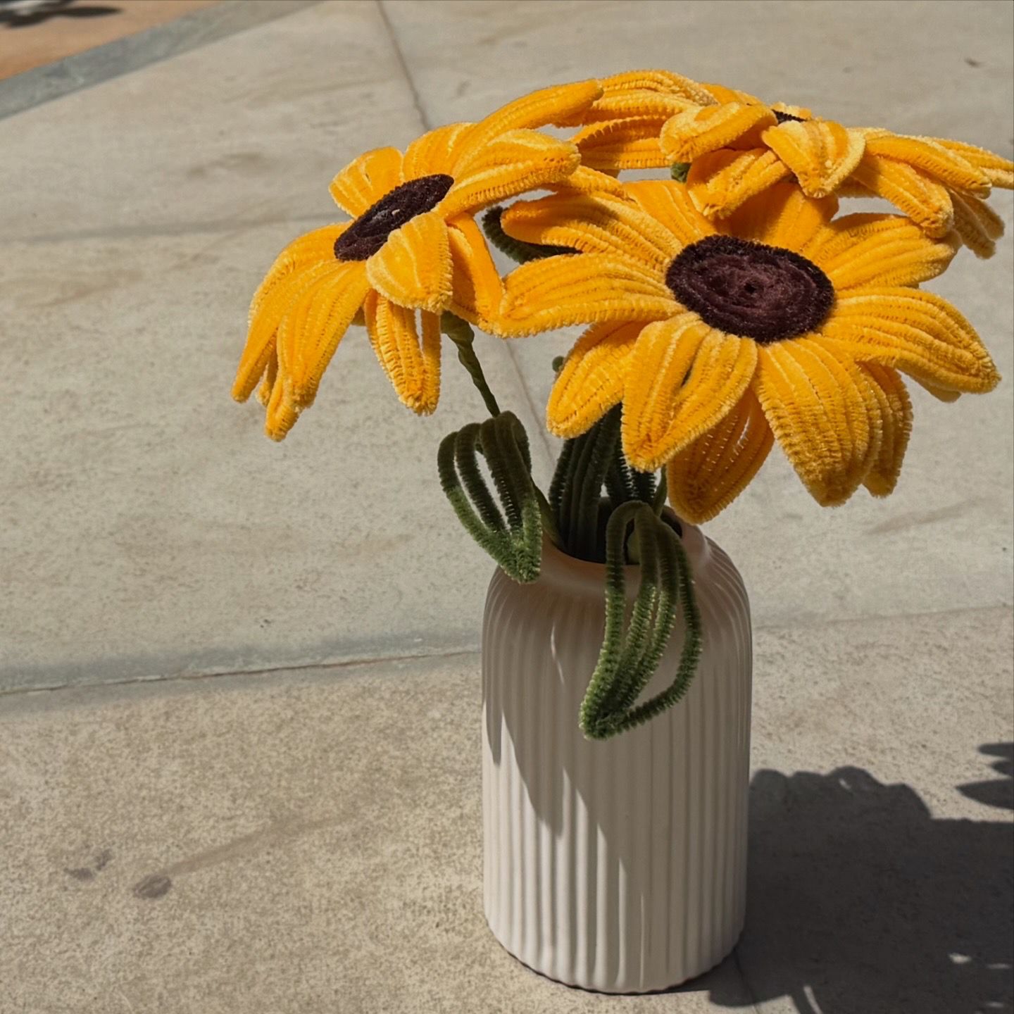 White vase with yellow sunflower-like flowers on a concrete surface
