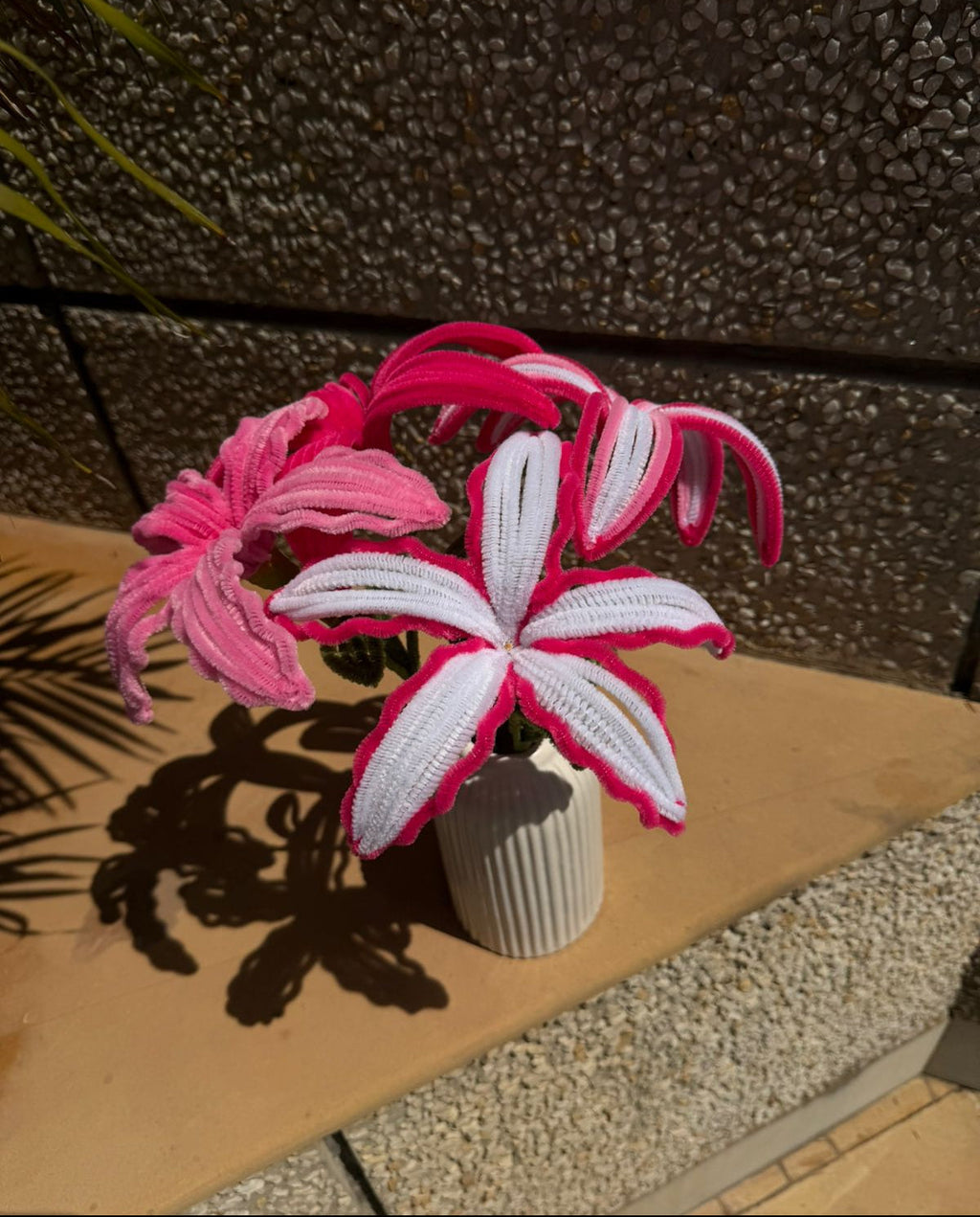 Decorative pink and white flower arrangement in a small pot on a stone surface.