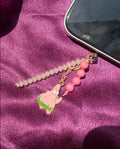 Phone charm with pink beads and a small figurine on a purple fabric background