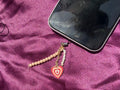Phone with a necklace draped over it on a purple fabric background