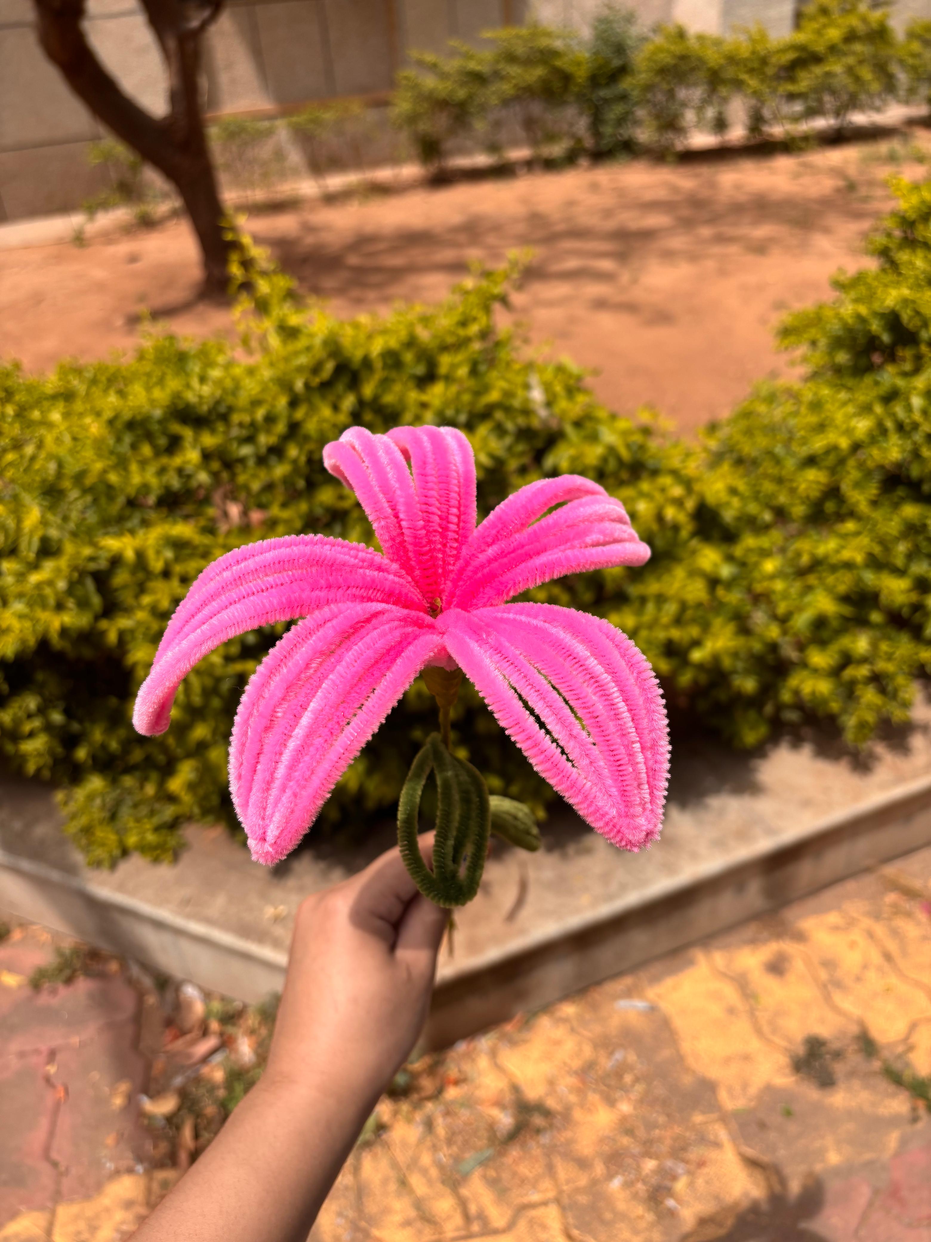 Pink artificial flower held by a hand with a garden background