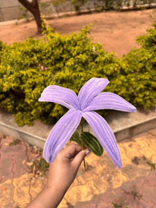 Hand holding a purple artificial flower with greenery in the background