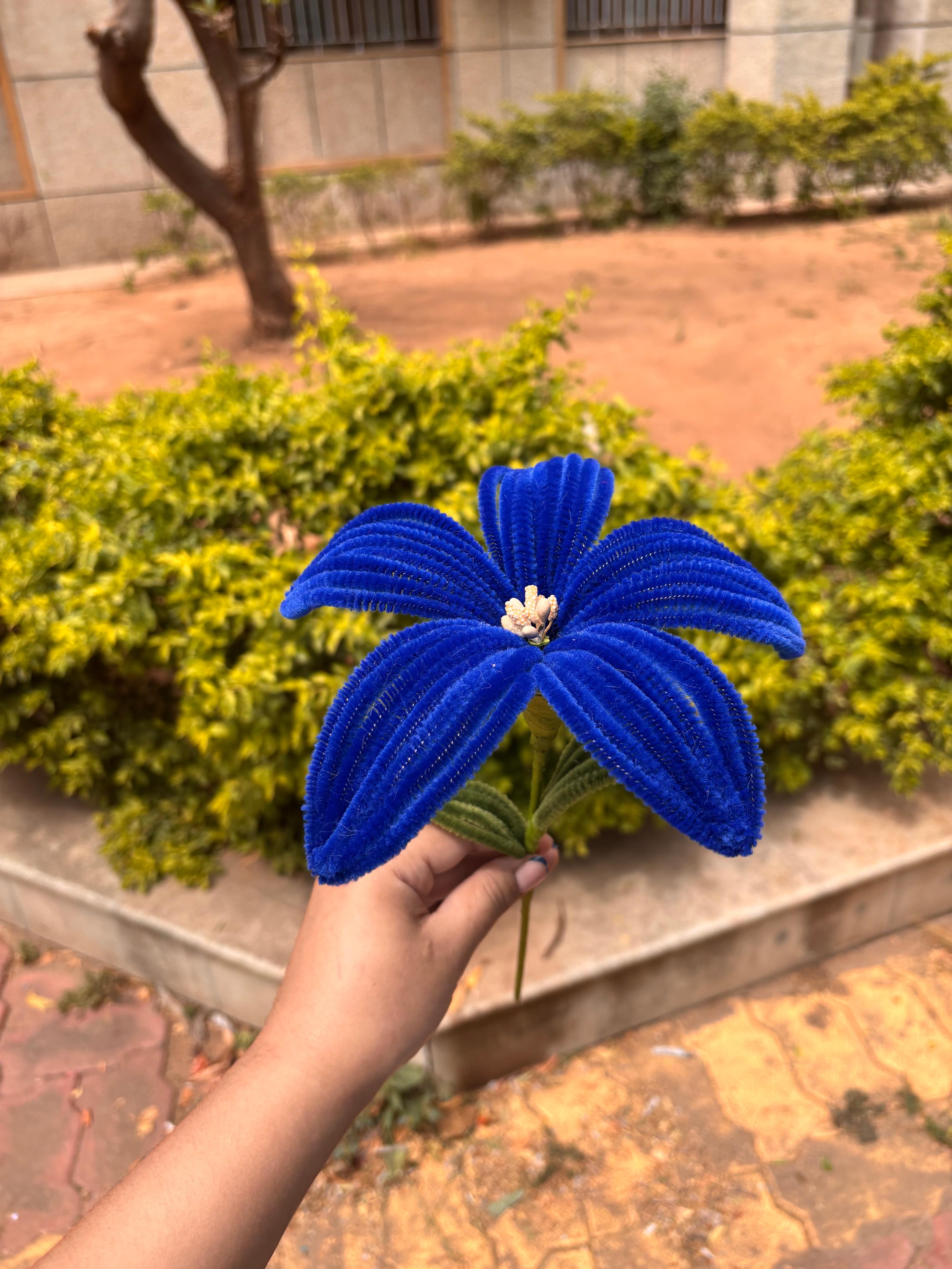 Blue artificial flower held by a hand with a garden background
