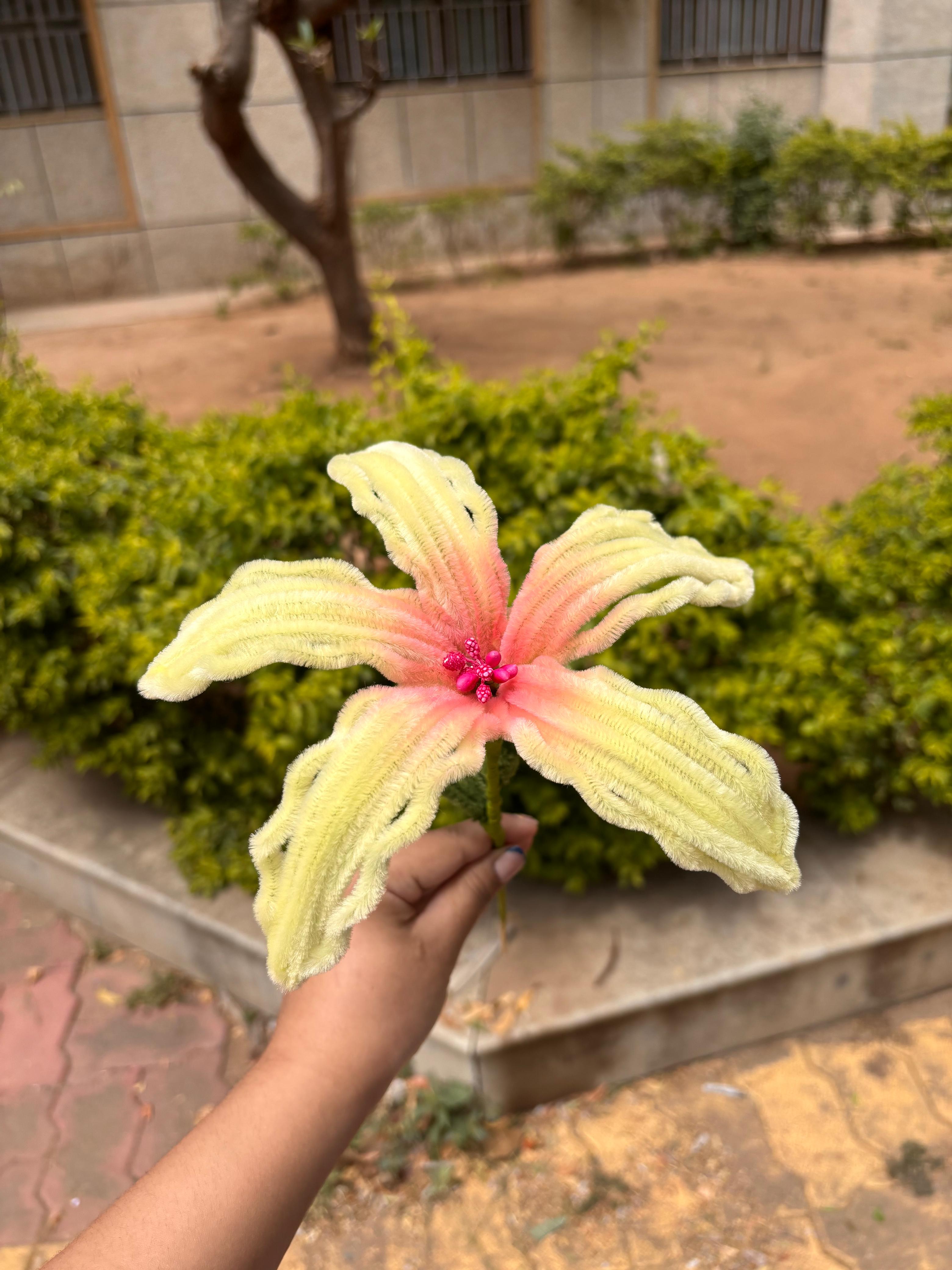 Large decorative flower held by a hand with greenery and a building in the background